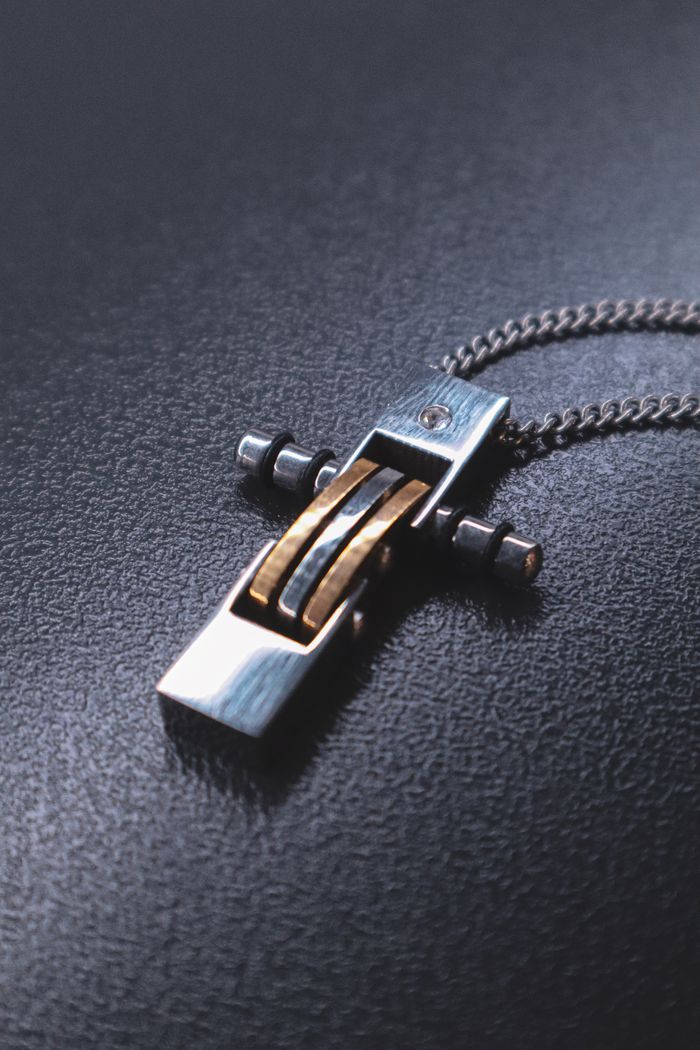 our-story-02 Sleek metallic cross pendant on a textured background, ideal for jewelry collections.